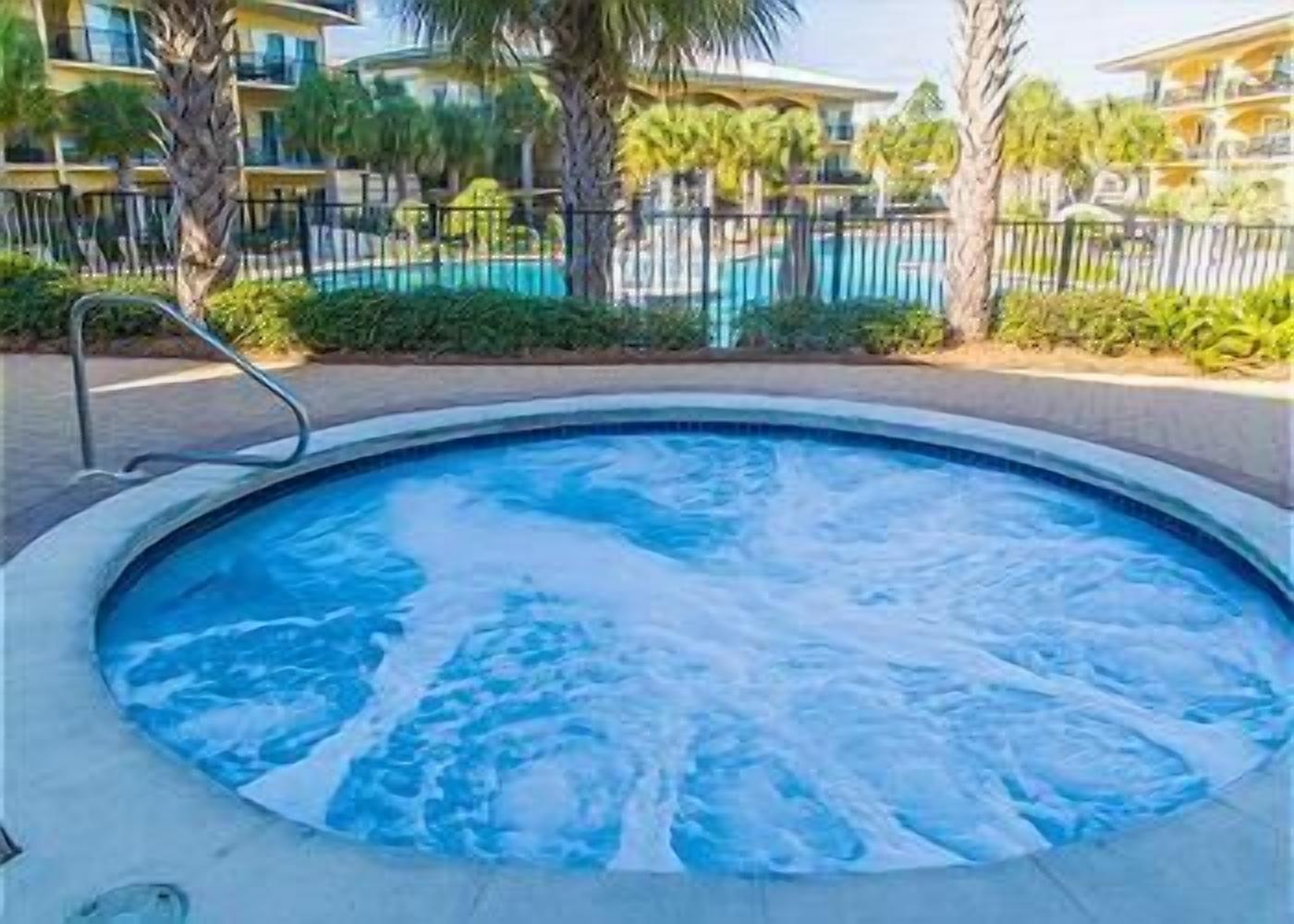 Una vasca idromassaggio circondata da una piscina, palme e un edificio con balconi.