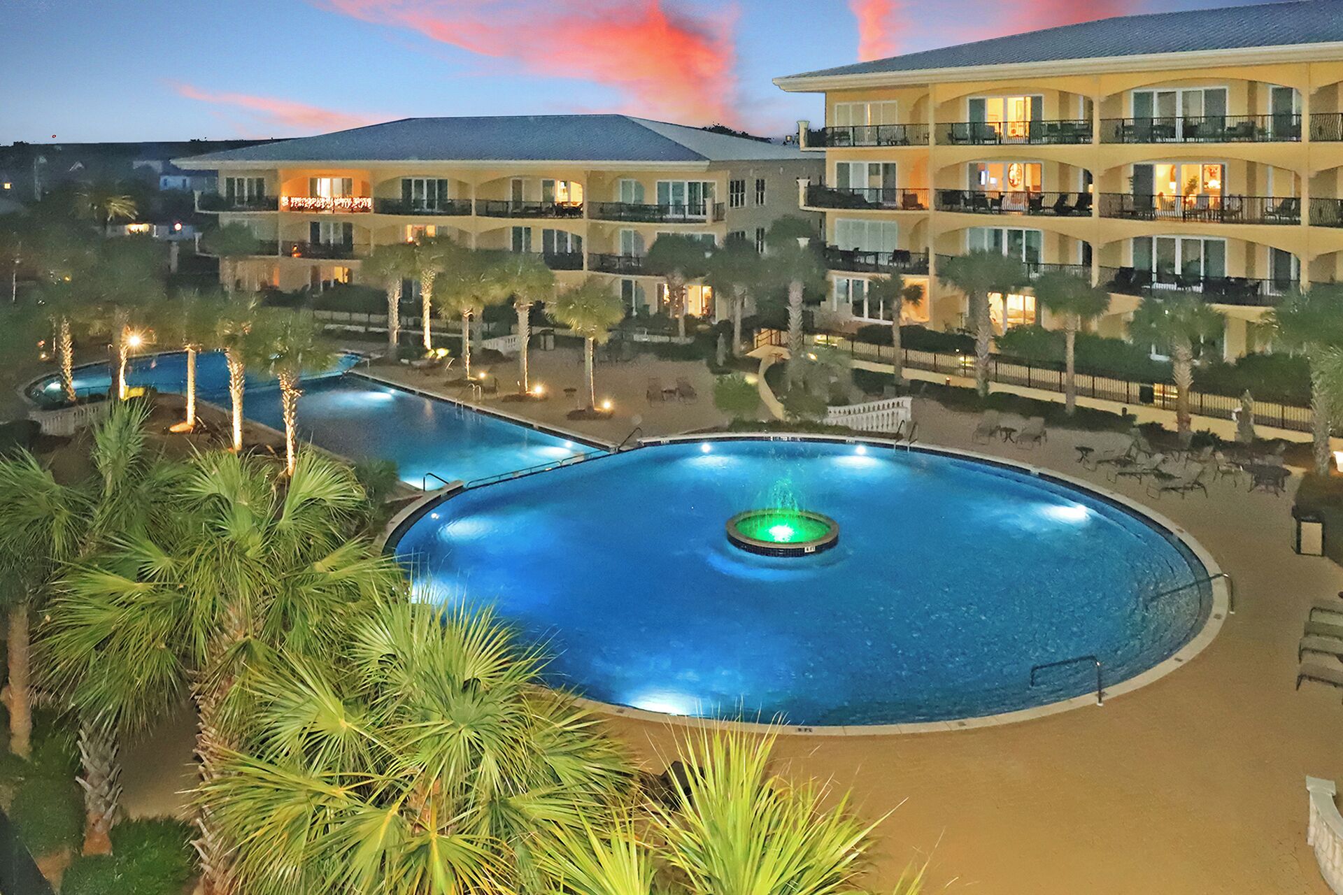 A resort with a large circular pool, palm trees, and a multi-story building with balconies.