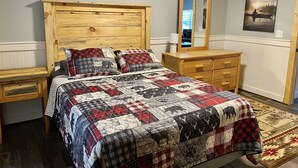 A bedroom with a wooden headboard, a bed with a quilt, a nightstand, a dresser, a mirror, and a rug. - Snowmobile Friendly! Ample Parking-only 1 block to trail! Clean w cozy Fireplace (AuTrain)
