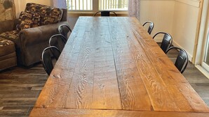 A dining area with a long wooden table, black chairs, a cushioned sofa, and a window with a view of a wooden deck. - Snowmobile Friendly! Ample Parking-only 1 block to trail! Clean w cozy Fireplace (AuTrain)