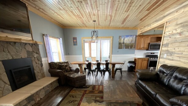 A spacious living room with a stone fireplace, wooden ceiling, and a dining area with a large table and chairs. - Snowmobile Friendly! Ample Parking-only 1 block to trail! Clean w cozy Fireplace (AuTrain)