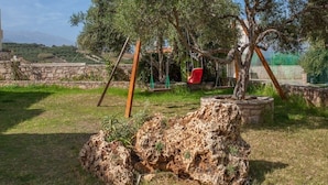 An outdoor area with a stone wall, a swing set, and a large tree. - Olive Tree Farm (Rethymno)