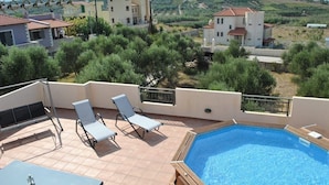A rooftop pool with two lounge chairs and a table, surrounded by olive trees and buildings in the background. - Olive Tree Farm (Rethymno)