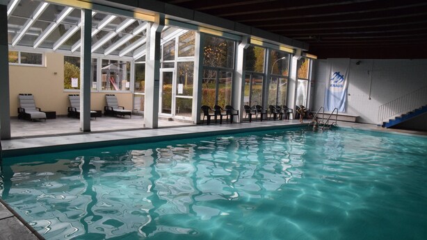 Una piscina interior con agua cristalina, una zona de estar techada con sillas y un cartel en la pared.