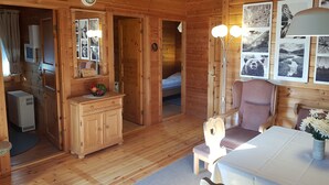 Acogedor interior de cabaña de madera con comedor, cocina equipada con lavaplatos y refrigerador, baño con ducha, y una cama en la habitación contigua.