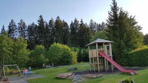 Un parque infantil con un tobogán de madera y una estructura para escalar, rodeado de césped y árboles.