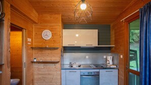 A compact kitchen with wooden walls, a clock, a sink, a stove, and a coffee maker.