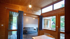 A wooden cabin interior with a sofa, a dining table, and large windows.