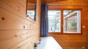A wooden cabin interior with a bench, two windows, and a curtain.