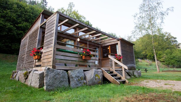 A wooden cabin with a porch, stone foundation, and potted flowers.