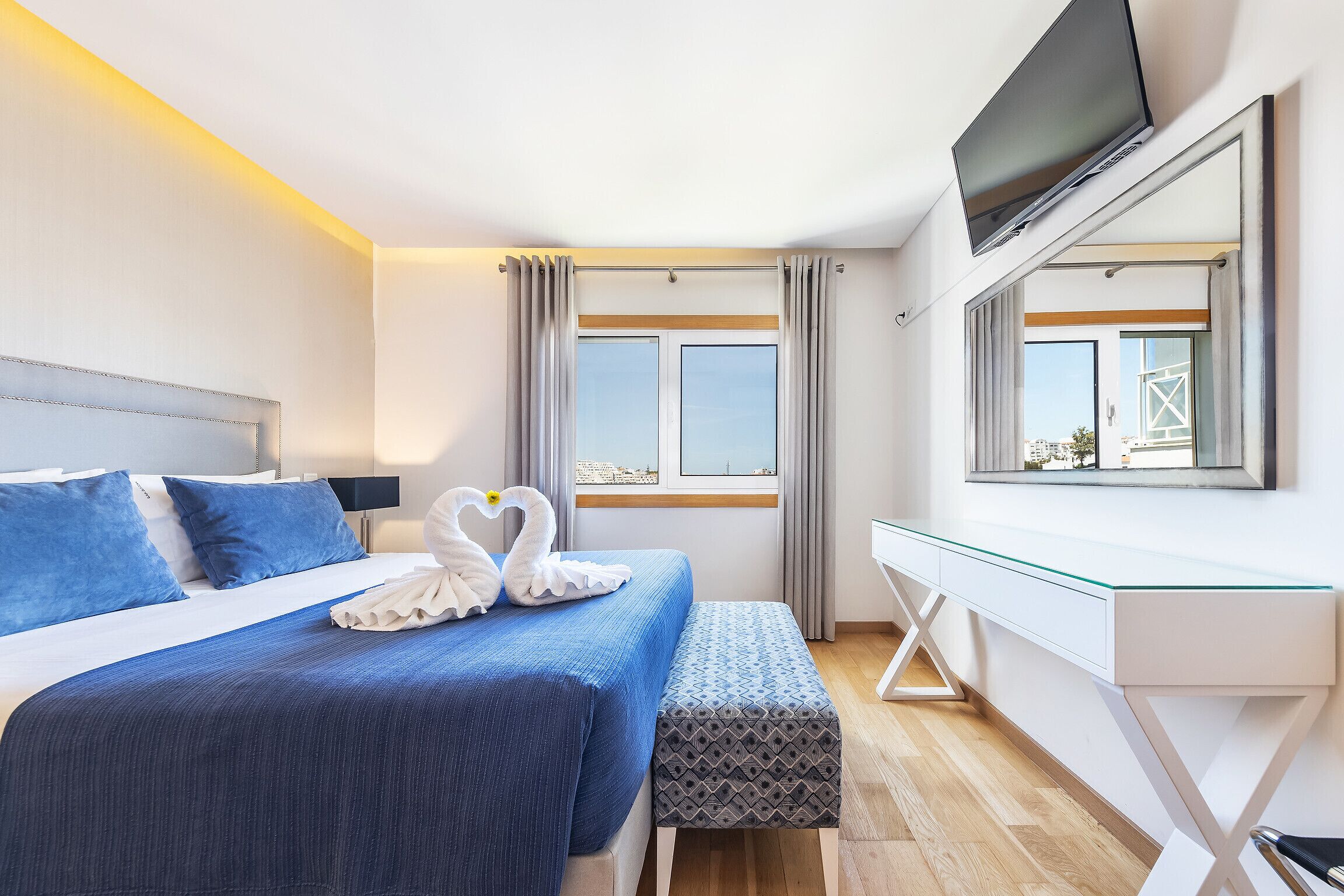 A modern hotel room with a bed, a desk, a TV, and a window with curtains.
