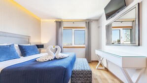 A modern hotel room with a bed, a desk, a TV, and a window with curtains. - Flat Old Town OCV - 3min Beach (Albufeira)