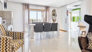 A modern living room with a dining area, a black armchair, and a view of the city through large windows. - Flat Old Town OCV - 3min Beach (Albufeira)
