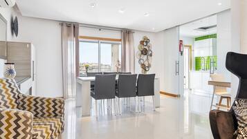A modern living room with a dining area, a black armchair, and a view of the city through large windows.