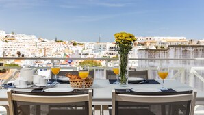 A dining table set with breakfast items, a vase of yellow flowers, and a view of a cityscape. - Flat Old Town OCV - 3min Beach (Albufeira)