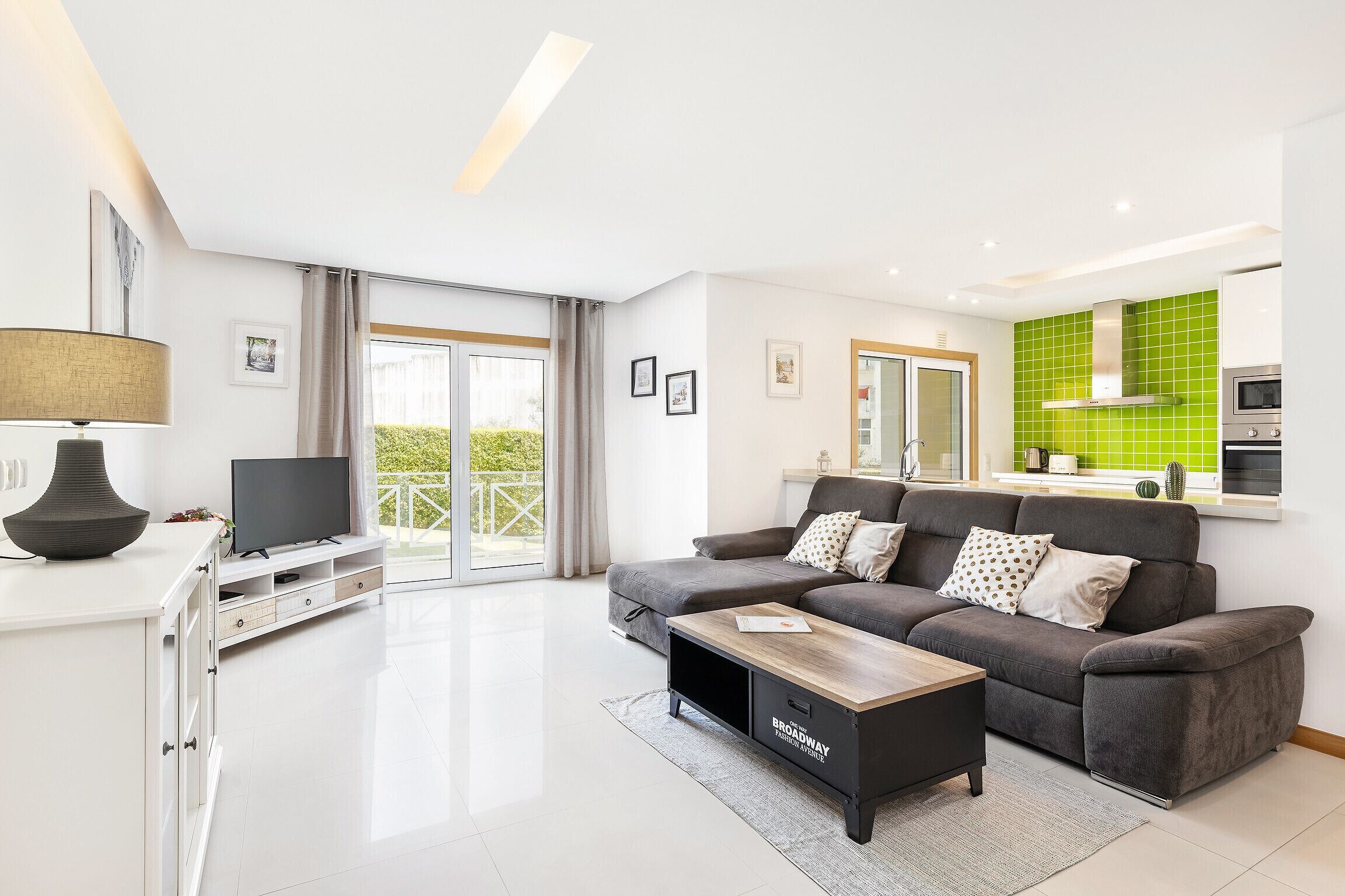 Een moderne woonkamer met een grijze bank, een flatscreen televisie en een houten salontafel.