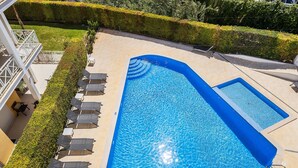 Ein rechteckiger Swimmingpool mit blauer Innenauskleidung, umgeben von einer gefliesten Liegefläche und einer Reihe von Liegestühlen.