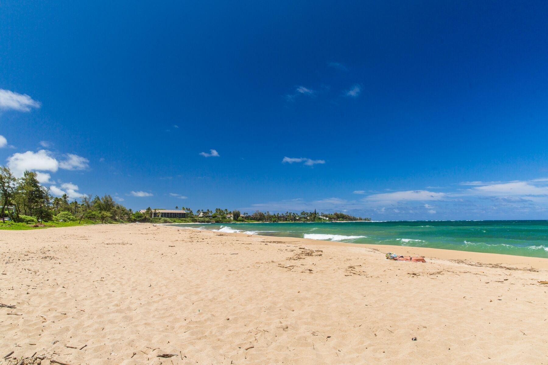 A wide sandy beach with clear turquoise waters and a few scattered clouds.