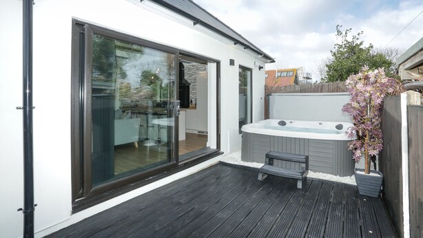 A modern outdoor deck with a hot tub, a bench, and a glass door leading to a kitchen area. - The Broadway Beach Homes Airbnb With Hot tub (Herne Bay)