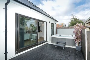 Um deck moderno ao ar livre com uma banheira de hidromassagem, um banco e uma porta de vidro que dá para uma cozinha.