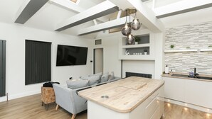 A modern kitchen with a wooden island, built-in shelves, and a flat-screen TV. - The Broadway Beach Homes Airbnb With Hot tub (Herne Bay)