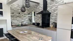 A modern kitchen with a central island, black range hood, and a tiled backsplash. - The Broadway Beach Homes Airbnb With Hot tub (Herne Bay)