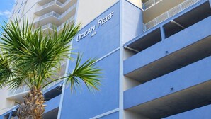 Un hotel de gran altura con un llamativo letrero que dice "Ocean Reef", varios balcones y una palmera en primer plano.