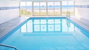 Una piscina interior con paredes de vidrio transparente, vista a la playa y un puesto de socorrista.