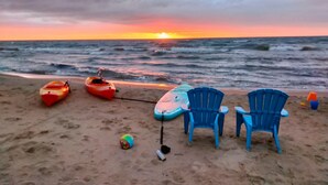 Una playa con kayaks, sillas, un voleibol y una tabla de surf.