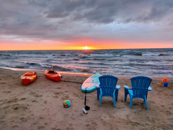 Une plage avec des kayaks et des chaises, un ballon de volley et une planche de surf.