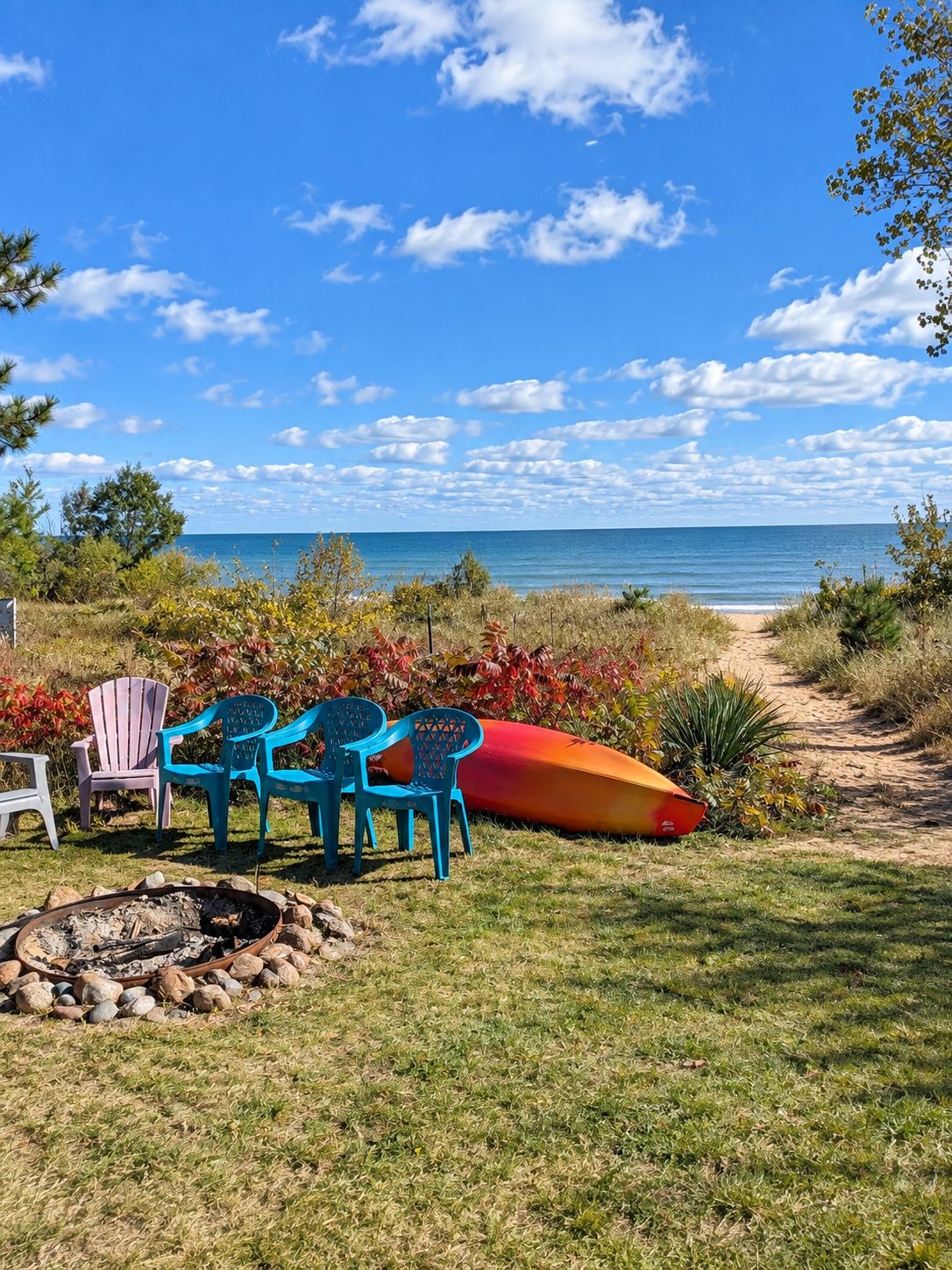 Un espace aménagé près de la plage, avec un foyer, des chaises et une planche de surf.