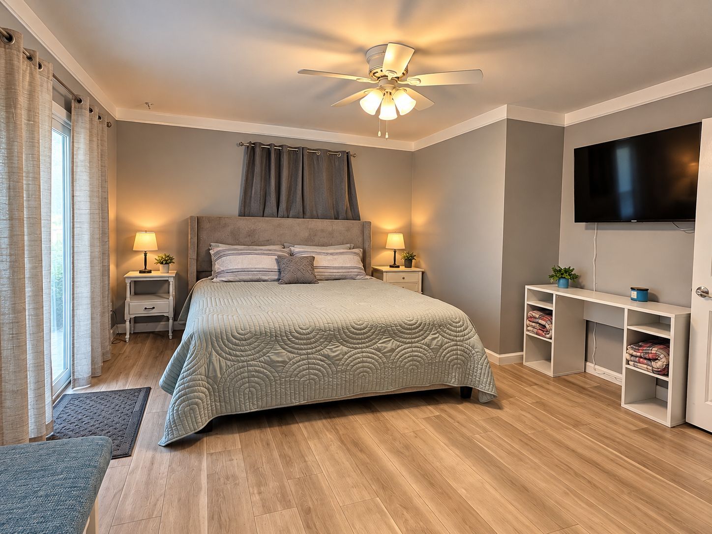 Une chambre à coucher comprenant un lit, des tables de chevet, un ventilateur de plafond, une télévision et une bibliothèque intégrée.