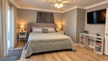 Une chambre à coucher comprenant un lit, des tables de chevet, un ventilateur de plafond, une télévision et une bibliothèque intégrée.