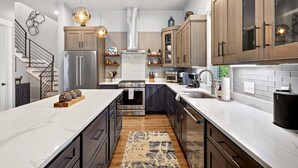 Une cuisine moderne dotée d’un îlot central, d’appareils électroménagers en acier inoxydable, de meubles en bois et de luminaires suspendus.