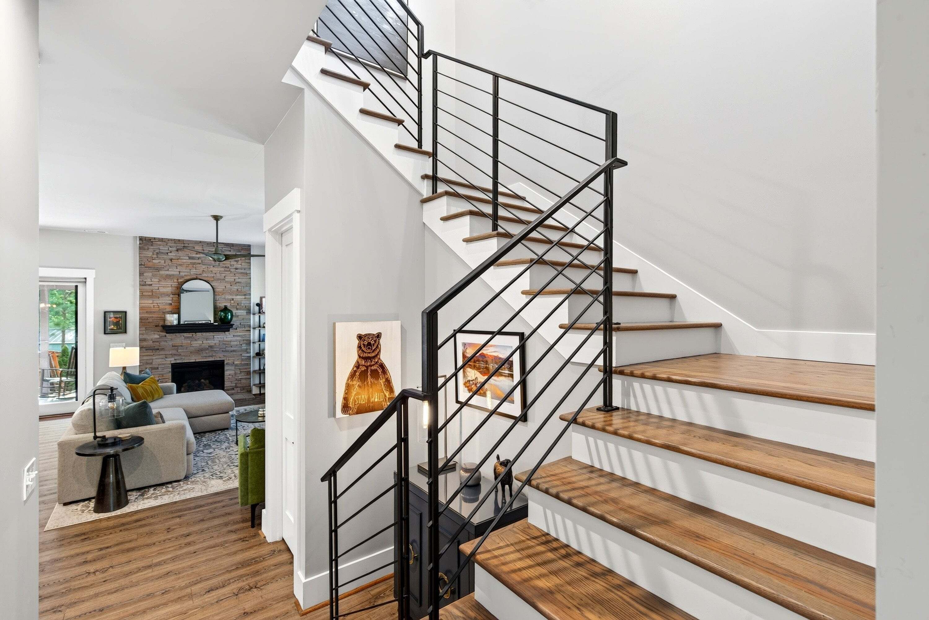 A staircase with wooden steps and black railings, leading to a living area with a fireplace and a sofa.
