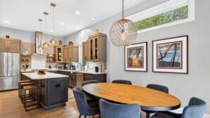 Une cuisine moderne dotée d’un îlot central, de tabourets de bar, de luminaires suspendus, d’œuvres d’art encadrées et d’une grande table à manger.