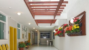 A clean, well-lit hallway with yellow chairs, potted plants, and hanging flower baskets. - Hotel Pousada Família de Nazaré (Cachoeira Paulista)