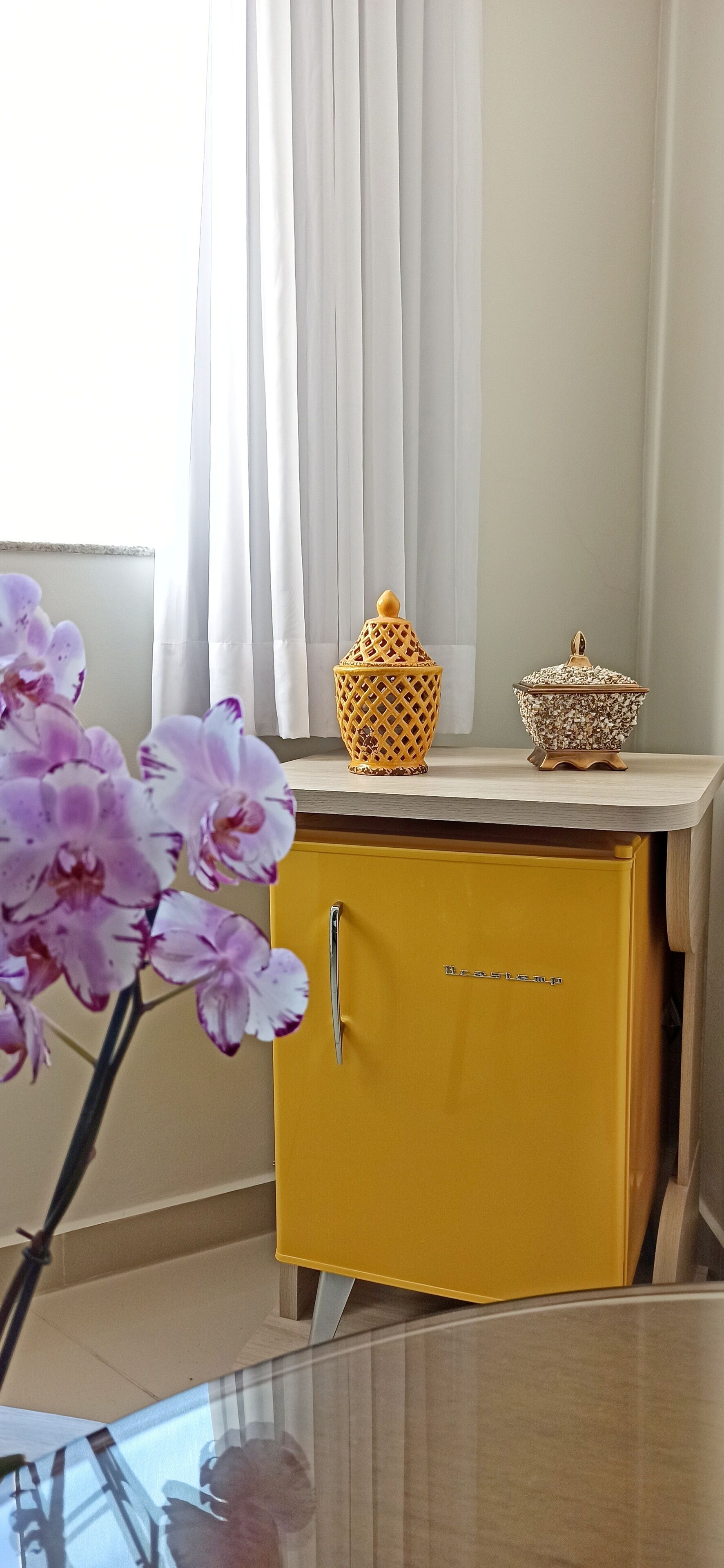 A yellow cabinet with a handle, a decorative container, and a vase with purple flowers on a table.