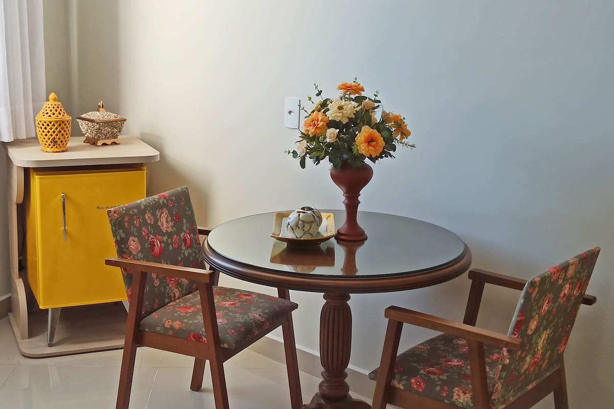 Ein Essbereich mit einem runden Tisch, zwei Stühlen, einem gelben Schrank und einer Blumenvase.