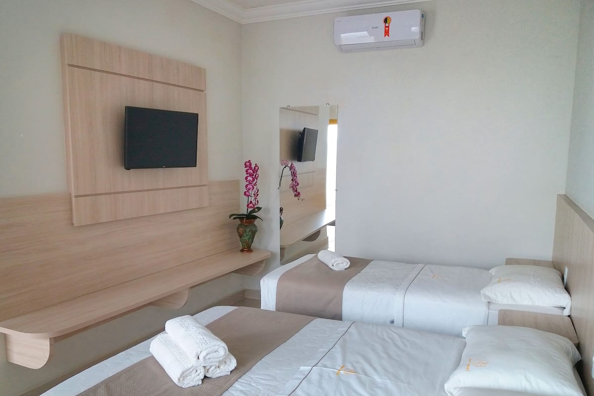 Ein Hotelzimmer mit zwei Betten, einem an der Wand montierten Fernseher und einem kleinen Tisch mit Blumenvase.