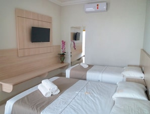 A hotel room with two beds, a TV mounted on the wall, and a small table with a vase of flowers. - Hotel Pousada Família de Nazaré (Cachoeira Paulista)