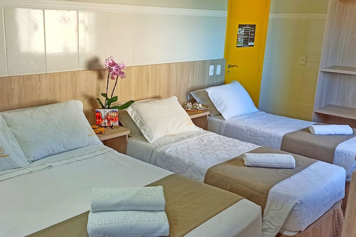 Ein Hotelzimmer mit zwei Betten, einem Holzkopfteil, einem kleinen Tisch mit Blumen in einer Vase und einer gelben Akzentwand.