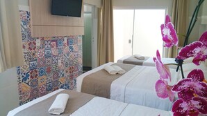 A hotel room with two beds, a television mounted on the wall, and a patterned tile wall. - Hotel Pousada Família de Nazaré (Cachoeira Paulista)