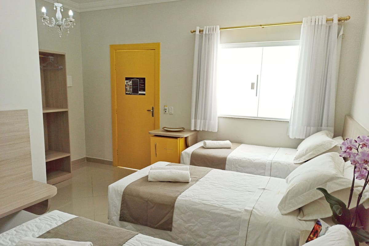 Ein Hotelzimmer mit zwei Betten, einem Holzschrank, einem kleinen Tisch und einem Fenster mit Vorhängen.