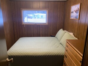 A bedroom with a bed, a dresser, a window with blinds, and a framed picture on the wall.