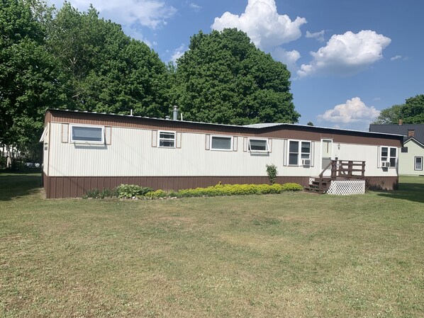 A mobile home with a brown exterior, white trim, and a small porch with a wooden railing.