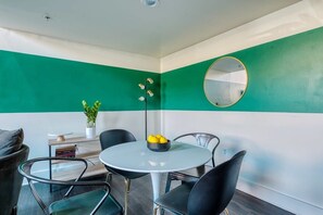 Uma área de refeições com uma mesa redonda, cadeiras pretas, uma planta em vaso e um espelho na parede.