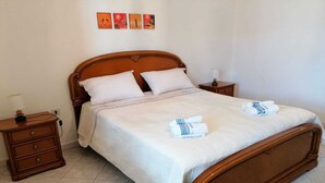 A neatly made bed with white linens and two towels folded on it, a wooden headboard, a nightstand with a lamp, and a wall with three framed pictures. - Spacious and lovely house (Orosei)