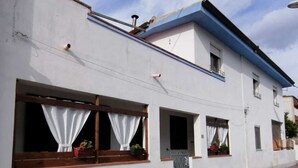 A two-story building with white walls and blue trim. There are three windows with curtains, and a small door with a metal gate. - Spacious and lovely house (Orosei)
