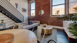 A modern living room with a brick wall, a staircase, and large windows.